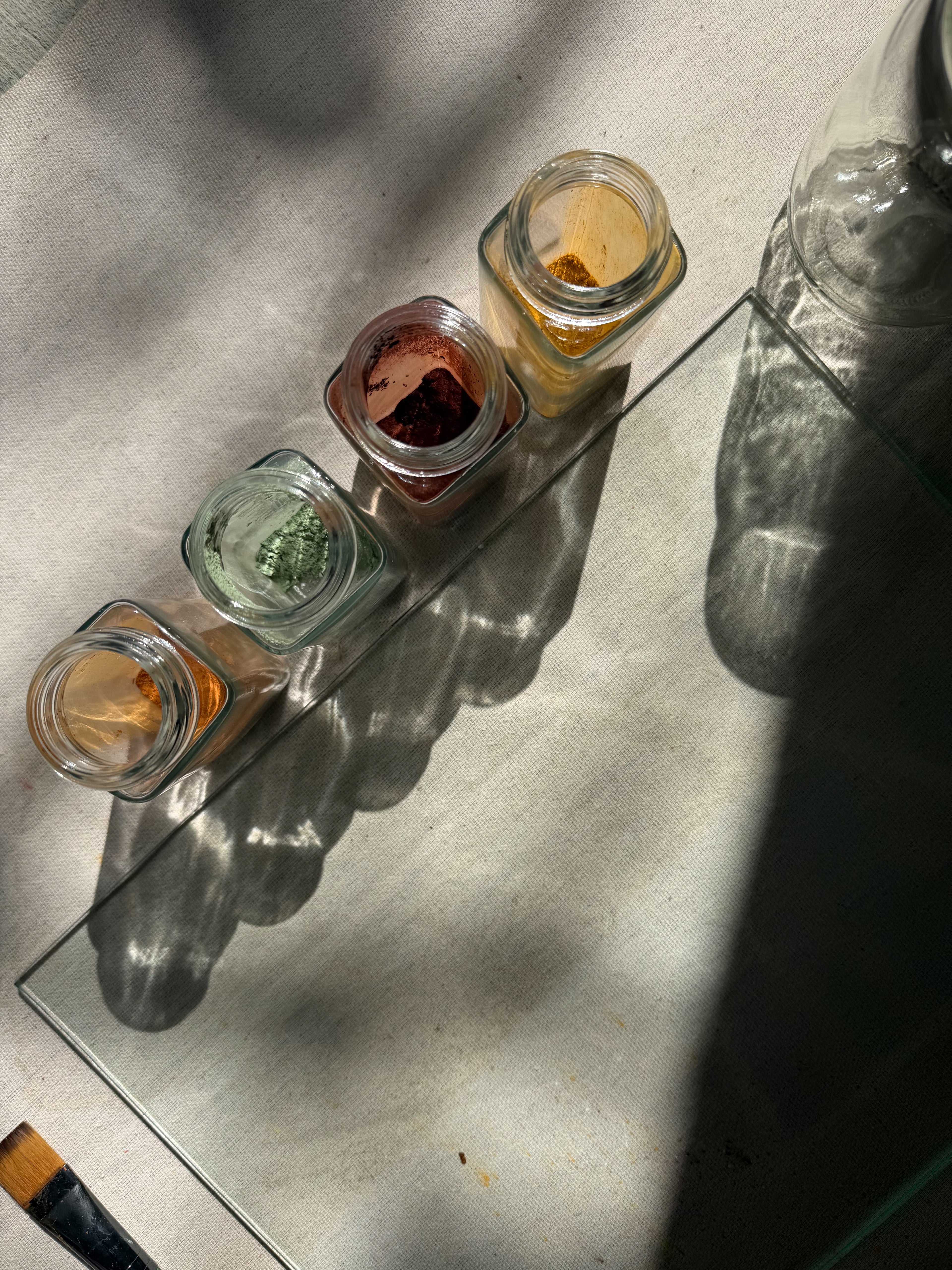 small glass jars with colorful earth pigments next to a glass palette and paintbrush 