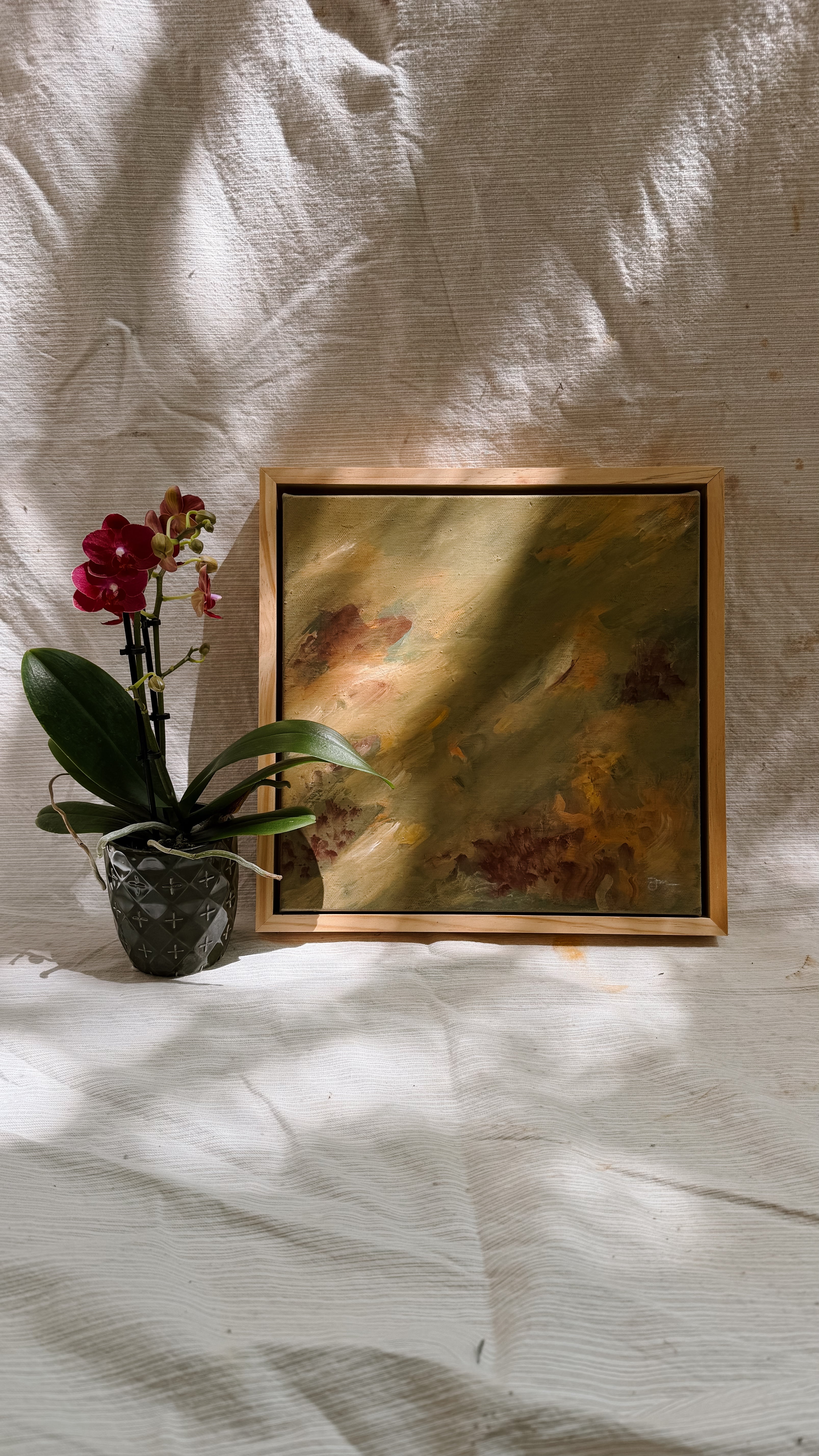 Framed abstract painting on a textured white wall with a potted orchid to the left.
